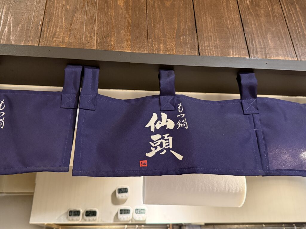 博多もつ鍋 仙頭 博多住吉店の外観写真。金曜21時、博多駅から徒歩12分の住吉エリアにある路面店の店構えで、塩もつ鍋の名店として知られる仙頭の入口と看板が夜の街並みに浮かぶ一枚