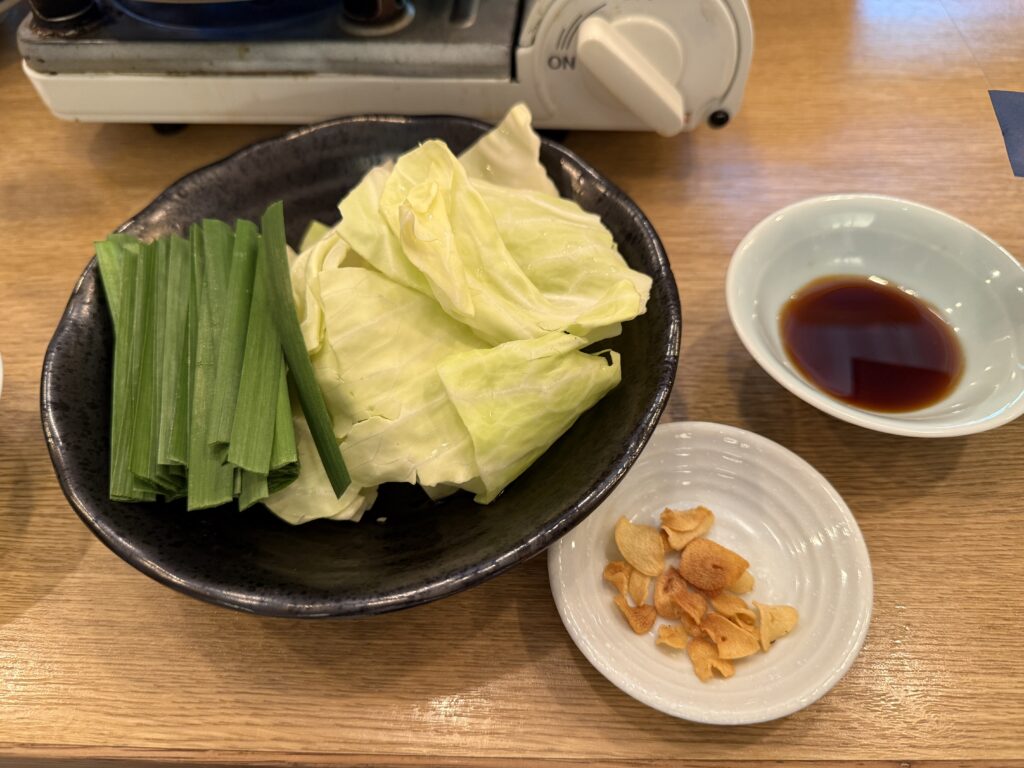 前田屋総本店の看板メニュー味噌もつ鍋を真上から捉えた一枚。プリプリのもつにキャベツ・ニラ・エノキ・こんにゃくが盛られ、にんにくと唐辛子が効いた濃厚な味噌スープが博多の王道を体現