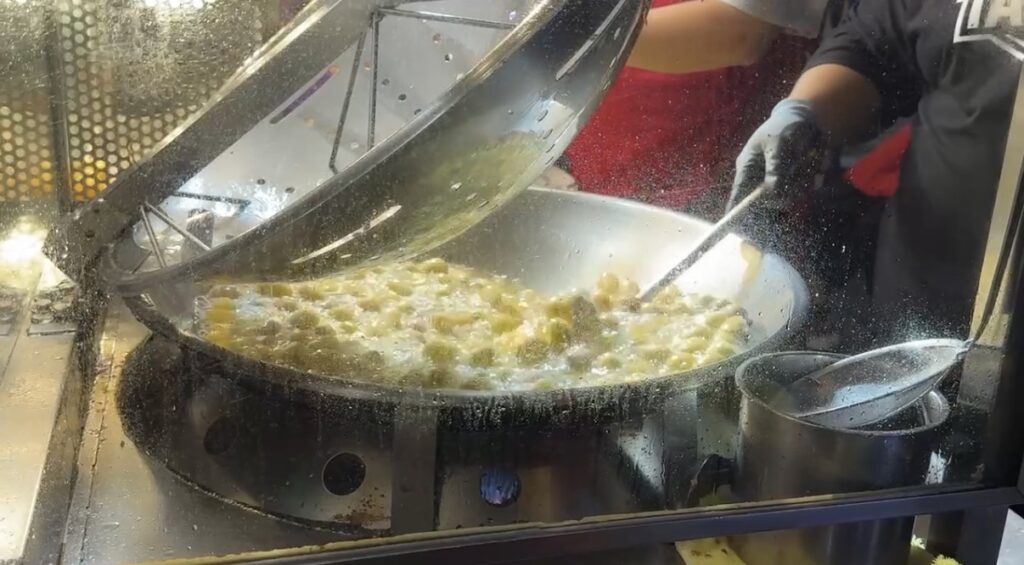 屋台の大鍋でこんがりと色づくまで揚げられている寧夏夜市名物のさつまいもボールを捉えた調理風景で、台北の夜市食べ歩きを象徴する熱々の揚げたて感と賑わいある屋台グルメの雰囲気が伝わる一場面