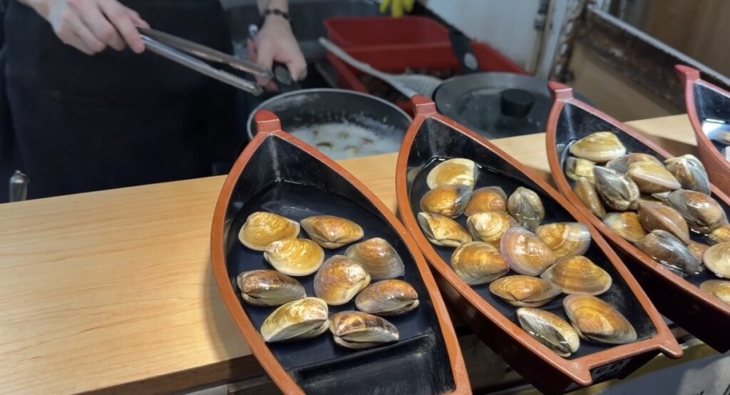 饒河街観光夜市の屋台で注文した蒸しはまぐりを器ごと写したカットで、貝が山盛りに盛られたボリュームのある一皿ながらスープがやや水っぽく見える様子が伝わり、台北夜市で屋台料理を選ぶ際の参考になる一枚