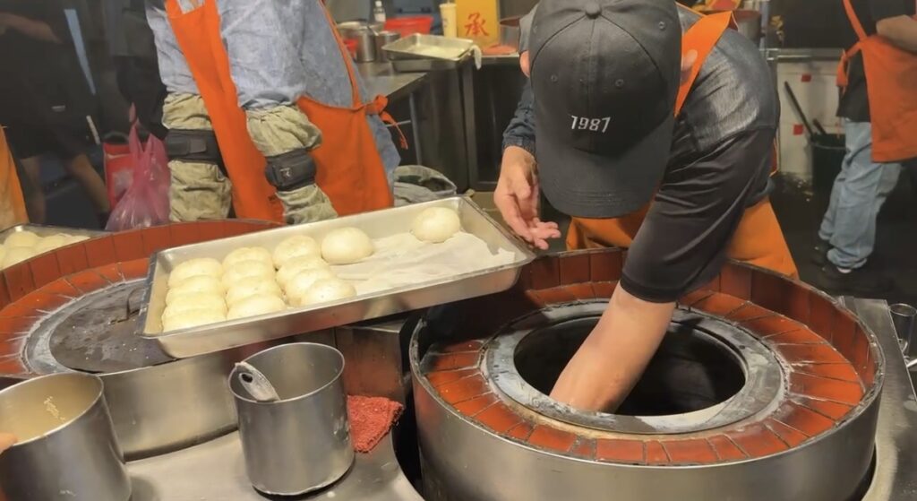 饒河街観光夜市の名物胡椒餅を実際に購入して撮影した一枚。こんがり焼き上がった生地の中に肉と胡椒の餡がぎっしり詰まり、ボリューム満点で食べごたえがある台北夜市グルメの代表格として人気の高さが伝わる横長カット